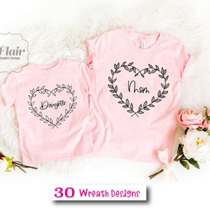 K&ouml;nnte beinhalten: Zwei rosa T-Shirts mit schwarzen floralen Herzdesigns. Das gr&ouml;&szlig;ere Shirt sagt "Mama" und das kleinere Shirt sagt "Tochter".