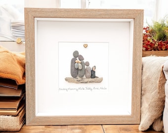 May include: Framed artwork featuring a family of five, crafted from smooth, gray stones. The figures are arranged on a piece of driftwood, with a small wooden heart above. The names "Daddy, Mommy, Moike, Teddy, Alvie, Nada" are written below.