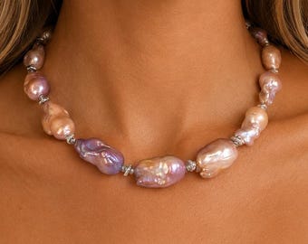 May include: A necklace featuring irregular, baroque-style pearls in shades of soft pink, lavender, and peach. The pearls are strung together with small, metallic silver-toned spacer beads, creating a continuous circular strand around the neck.