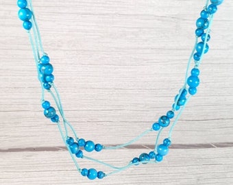 May include: A triple-strand necklace with turquoise blue beads on a light blue cord.