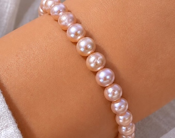 May include: A bracelet composed of round, light pink pearls. The pearls are strung together, forming a continuous loop. The bracelet is worn on a wrist, showcasing the delicate color and luster of the pearls.