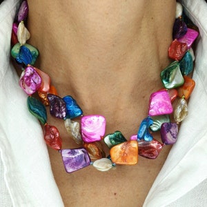 May include: A vibrant necklace with iridescent, irregularly shaped beads in pink, green, blue, orange, and purple. The necklace has two strands and is worn around the neck.