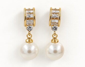 May include: A pair of gold-toned drop earrings featuring a curved top section set with clear baguette-cut stones, a single round clear stone below, and a dangling white spherical pearl at the base of each earring.