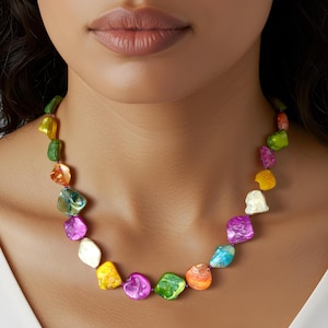May include: A vibrant necklace with irregularly shaped, iridescent beads in shades of green, yellow, purple, orange, and blue. The beads are strung together, creating a colourful accessory. This statement necklace would be a great addition to any outfit.