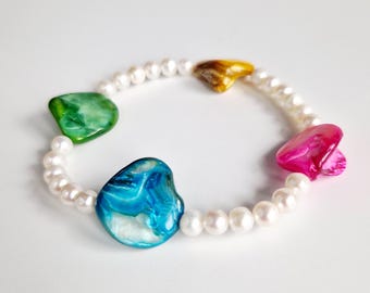 May include: A stretch bracelet featuring white pearls and colorful, irregularly shaped shell beads. The shell beads are in shades of green, blue, gold, and pink. The bracelet is designed to be worn around the wrist.