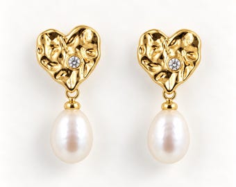 May include: A pair of gold-toned earrings featuring a textured heart-shaped stud with a single embedded clear stone, from which a smooth, white, teardrop-shaped pearl hangs. The design combines a metallic, hammered finish with a classic pearl.