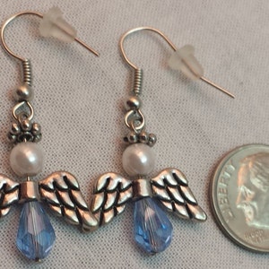 May include: A pair of silver angel wing earrings with a white pearl and a light blue crystal bead on each earring.