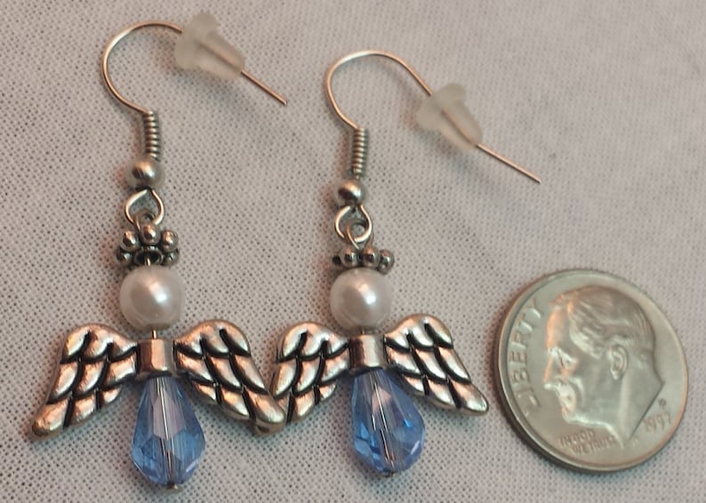May include: A pair of silver angel wing earrings with a white pearl and a light blue crystal bead on each earring.