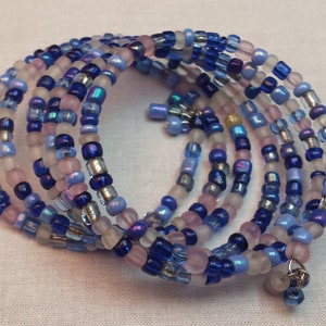 May include: A multi-strand wrap bracelet composed of small, colorful beads. The bracelet features a mix of blue, purple, silver, and pink beads. The beads are strung together to create a spiral design, with a small charm hanging from the end.