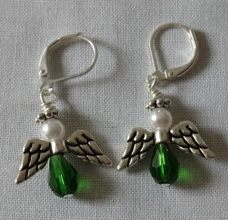 May include: A pair of silver angel earrings with green crystal accents and white pearl beads.