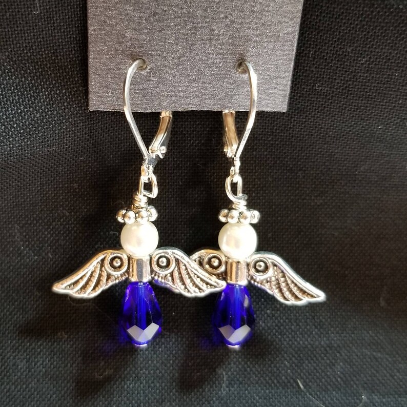 May include: Silver angel wing earrings with a white pearl and a dark blue crystal dangle.