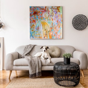 Könnte beinhalten: Ein weißer Hund mit schwarzen Flecken sitzt auf einem grauen Sofa in einem Wohnzimmer. Das Sofa hat eine graue Wolldecke und ein beigefarbenes Kissen. Vor dem Sofa steht ein schwarzer Korbtisch mit einer Topfpflanze darauf. Die Wand hinter dem Sofa ist weiß und hat ein großes abstraktes Gemälde.