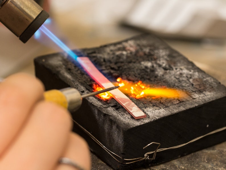 May include: A person uses a torch to heat a piece of metal on a black surface. The metal is glowing red hot and the torch is producing a bright orange flame.