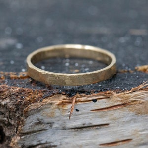 May include: A simple gold band ring with a hammered texture. The ring is sitting on a piece of wood.