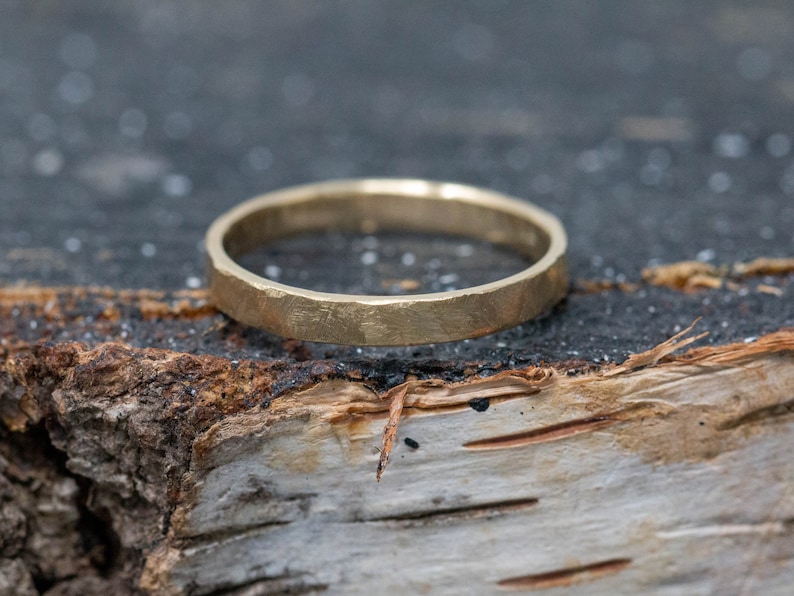 May include: A simple gold band ring with a hammered texture. The ring is sitting on a piece of wood.