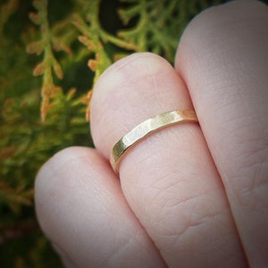 May include: A simple gold band ring with a hammered texture. The ring is worn on a finger.