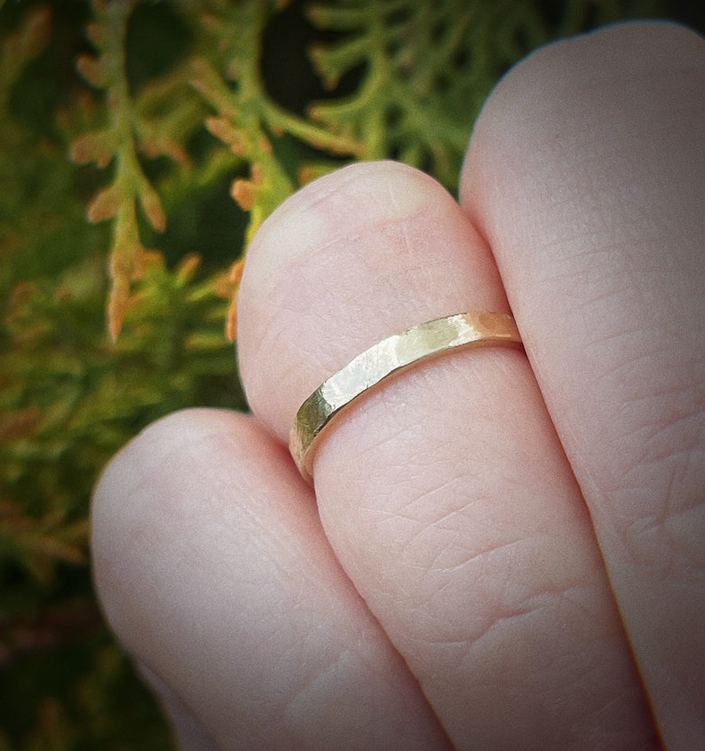 May include: A simple gold band ring with a hammered texture. The ring is worn on a finger.