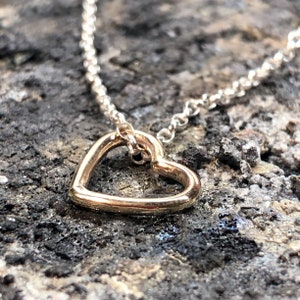 May include: A delicate silver chain necklace with a simple gold heart pendant.