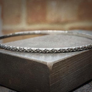 May include: A silver bangle bracelet with a geometric pattern around the edge.