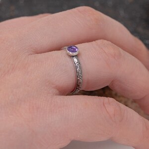 May include: A silver ring with an intricate design and a small purple gemstone.