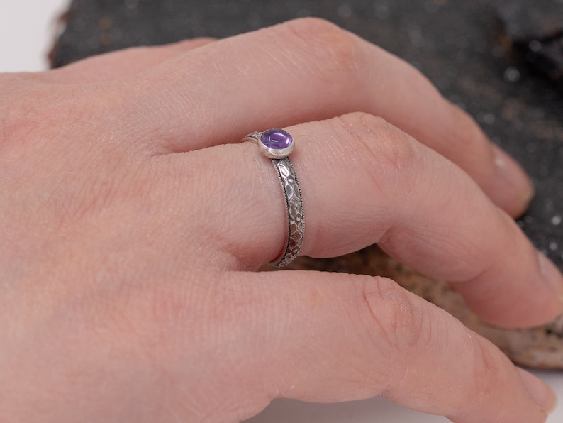 May include: A silver ring with an intricate design and a small purple gemstone.