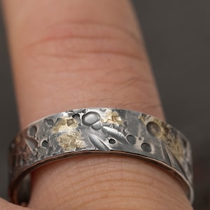 May include: A silver and gold band ring with a textured surface. The ring has a hammered finish and is decorated with small gold accents.