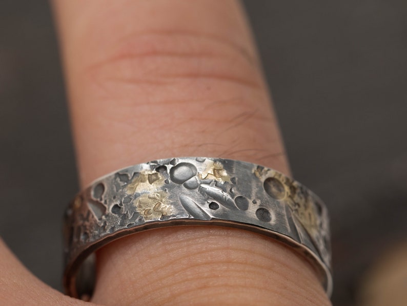 May include: A silver and gold band ring with a textured surface. The ring has a hammered finish and is decorated with small gold accents.