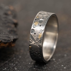 May include: A silver ring with a textured surface and gold accents. The ring has a hammered finish and a unique design.