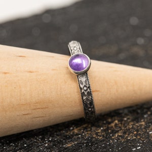 May include: A silver ring with a purple gemstone set in a floral design.
