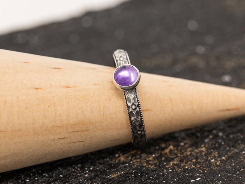 May include: A silver ring with a purple gemstone set in a floral design.