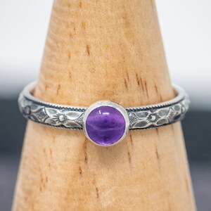 May include: A silver ring with an intricate floral design and a purple amethyst gemstone.