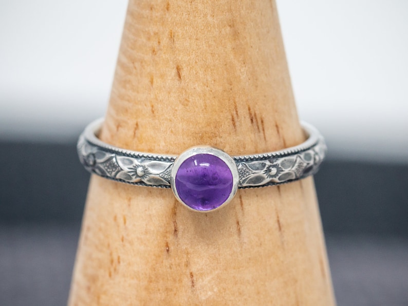 May include: A silver ring with an intricate floral design and a purple amethyst gemstone.