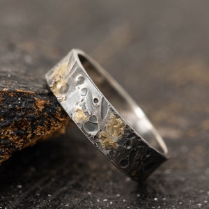 May include: A silver ring with a textured surface and gold accents. The ring has a hammered finish and a unique design.