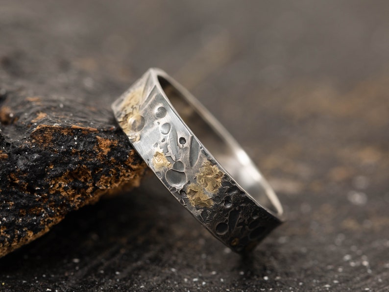 May include: A silver ring with a textured surface and gold accents. The ring has a hammered finish and a unique design.