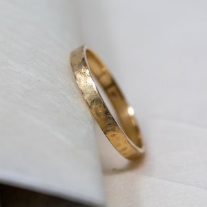 May include: A simple gold band wedding ring with a hammered texture.