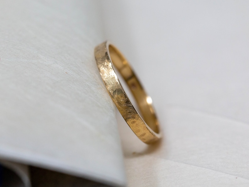 May include: A simple gold band wedding ring with a hammered texture.
