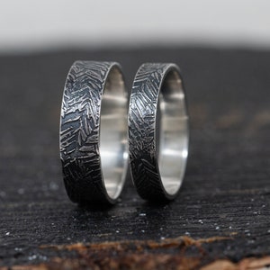 May include: Two silver wedding bands with a textured, brushed finish. The bands are stacked on top of each other.