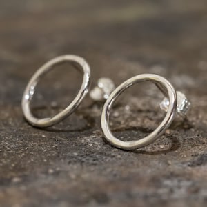 May include: A pair of silver circle earrings with a hammered texture. The earrings are simple and modern.