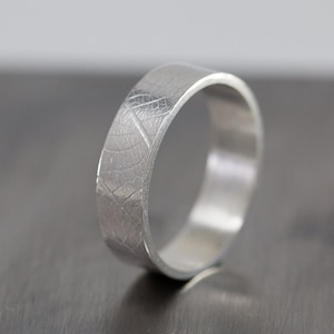May include: A silver ring with a textured leaf design. The ring is wide and has a polished finish.