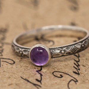 May include: A silver ring with an ornate floral design and a purple amethyst gemstone.
