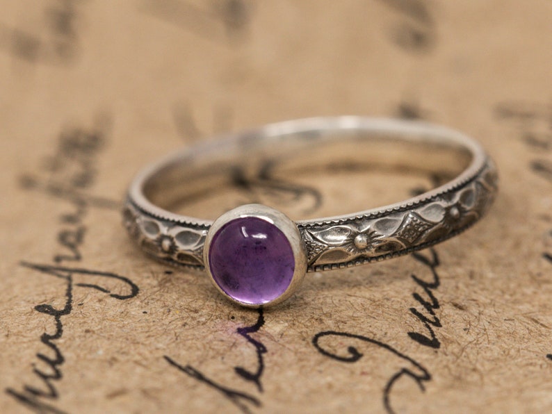 May include: A silver ring with an ornate floral design and a purple amethyst gemstone.