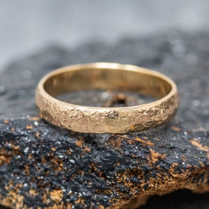 May include: A gold wedding band with a textured hammered finish. The band is simple and elegant, with a subtle shine.
