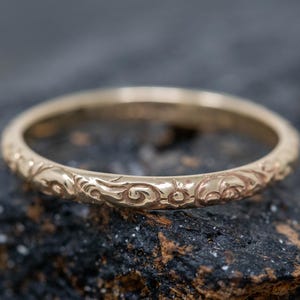 Könnte beinhalten: Ein dünner Goldring mit einem zarten floralen Design, das um den gesamten Umfang graviert ist.