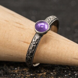 May include: A silver ring with a floral design and a purple gemstone.