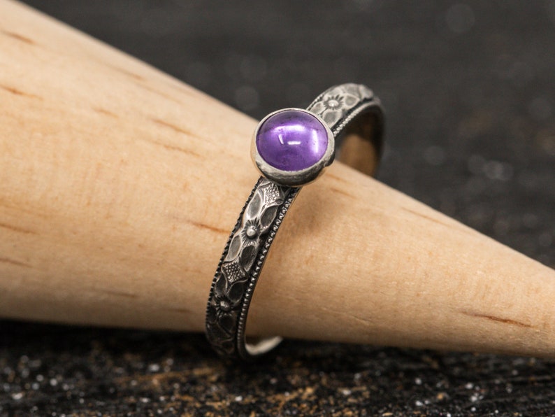 May include: A silver ring with a floral design and a purple gemstone.