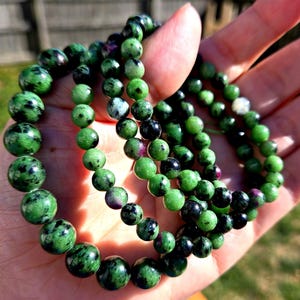 Puede incluir: Tres pulseras de piedras preciosas verdes y negras con cuentas redondas. Las pulseras están hechas de aventurina verde con motas negras.