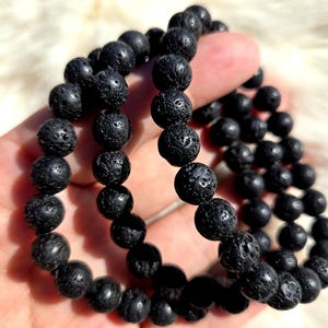 Puede incluir: Tres pulseras de cuentas de roca de lava negra apiladas una encima de la otra.