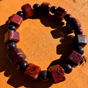 May include: A red and black beaded bracelet with square-shaped red beads and round black beads.