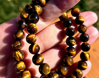 May include: Two brown and gold tiger's eye beaded bracelets. The beads are round and have a shiny, polished finish.