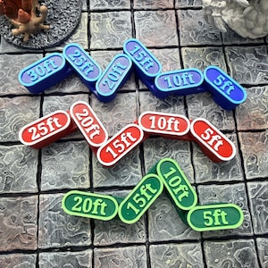 Könnte beinhalten: Eine Ansammlung von gebogenen Spielmarken in Blau, Rot und Grün, die jeweils mit Entfernungen in Fuß beschriftet sind: 5ft, 10ft, 15ft, 20ft, 25ft und 30ft. Die Spielmarken liegen auf einer strukturierten, grauen Oberfläche.